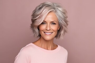Portrait of a beautiful mature woman smiling at the camera while standing against a pink background