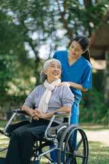 Smiling physiotherapist taking care of the happy senior patient in wheelchair, outdoor.