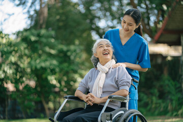 Smiling physiotherapist taking care of the happy senior patient in wheelchair, outdoor.