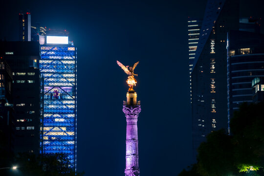 Illuminated view of night Mexico city with glowing The Angel of Independence statue placed among tall skyscrapers in evening Mexico city