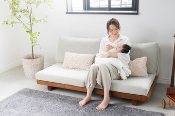 ソファーに座って赤ちゃんにミルクをあげる女性の全身の広角...