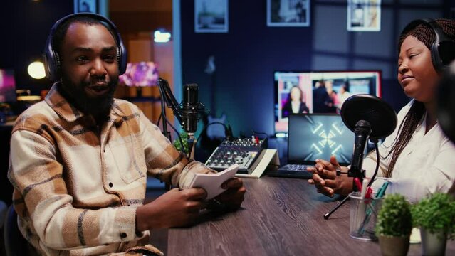 BIPOC man on podcast conversating with guest during marathon stream for charitable cause. Host in apartment studio chatting with celebrity, gathering donations from fans during online show