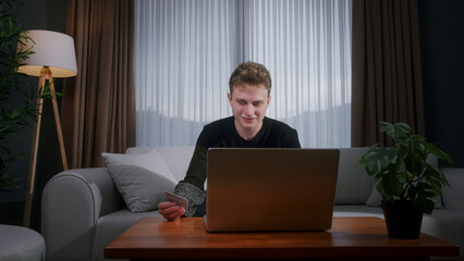 Young blonde man sitting enter credit card number on laptop for makes secure easy distant...