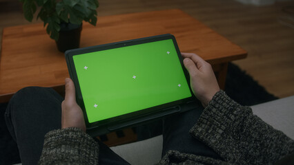 Young man scrolling and tapping center on tablet with green screen mock up display. Male sitting on...