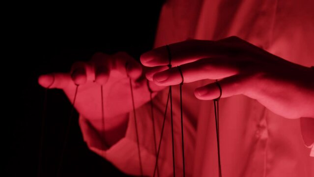 The puppeteer controls the puppets in the theater in red neon light close-up. Managing people at work, in politics and government. Action control