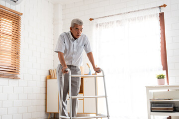 Asian Senior elderly man patient walking slowly with walker in house. 