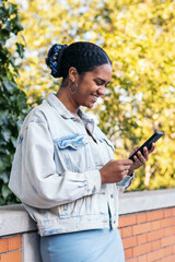 Fototapeta premium African-American girl using a smartphone in the park on a summer day.