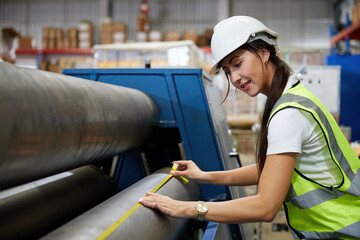 female factory worker using tape measure and measuring the length of the steel pipe in the factory