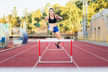 Obraz premium An athletic woman jumping hurdles on an athletics track.