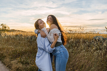 two young women hugging on a field during sunset