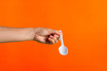 White plastic spoon in hand on orange background