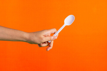 White plastic spoon in hand on orange background