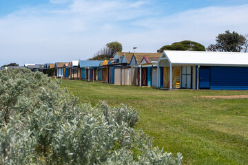 Fototapeta na wymiar A row of colorful beach huts with diverse designs stands on a grassy field. Werribee South, Melbourne VIC Australia.