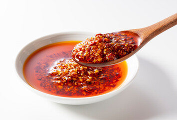 Edible chili oil in a ceramic dish set against a white background. Scooped up with a wooden spoon....