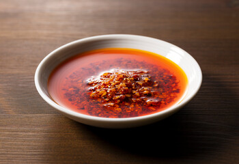 An edible chili oil in a ceramic dish placed on a wooden background.