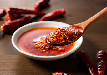 An edible chili oil in a ceramic dish placed on a wooden background. Scooped up with a wooden...