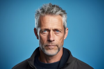 Portrait of senior man with grey hair and blue eyes on blue background