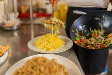 Cook plating vegetables noddles in a counter of a restaurant