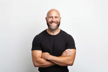 Fotobehang Portrait of a happy bald man in a black t-shirt with crossed arms © Inigo