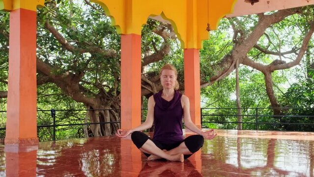Mindfulness caucasian woman meditates sitting on the floor in indian temple outdoors. She puts her hands in mudra namaste. Female practice for wellbeing and mental health.