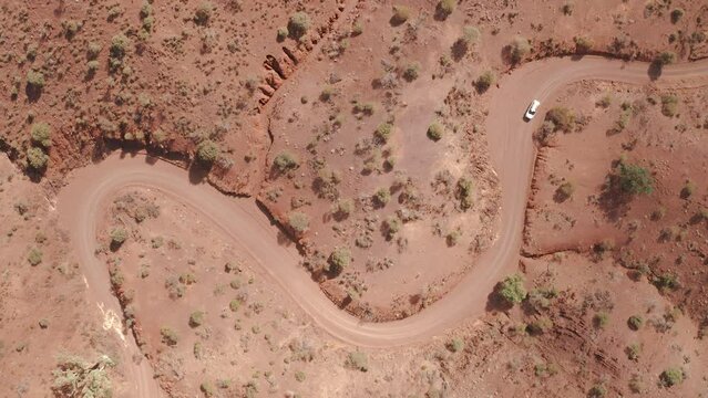 Bird's eye view of white car driving on winding dirt road in Flinders Ranges, South Australia