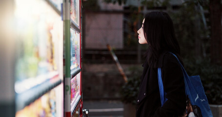 Travel, food and hot drink vending machine with Japanese woman choosing snack to purchase in the dark. Night, hunger and choice with young tourist looking at product options for journey Tokyo city