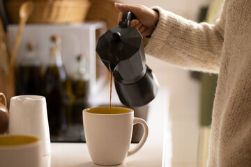 Hand of a woman pouring coffee with an italian coffee maker in a kitchen