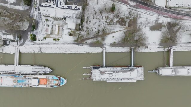 Ships and boats anchored by the river near city park. Aerial top down view.