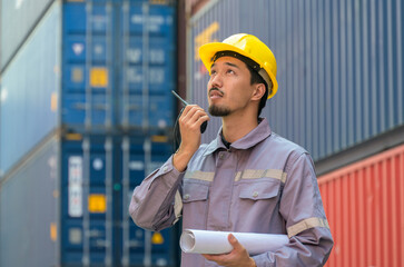 Portrait of Japanese engineer wearing protective helmet and holding blueprint while talking on...