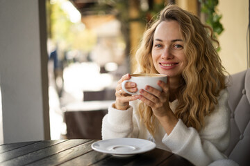 Beautiful happy blonde woman with long curly hair enjoying coffee in cafe