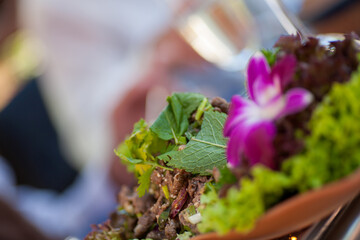 The photograph is a close-up of a gourmet salad presented in a terracotta bowl, garnished with a...