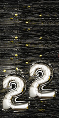 Silver foil balloon number 22 on a background of black tinsel decoration with golden confetti. Birthday greeting card, inscription twenty-two. Anniversary event. Vertical Banner.