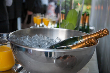 The photograph captures an elegant setting, likely at a social gathering or celebration, where a bottle of champagne rests in a bed of ice within a metallic bowl. The ice glistens, reflecting the