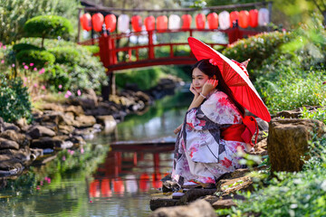 Obraz premium A young woman wearing a Japanese traditional kimono or yukata holding an umbrella is happy and cheerful in the park.
