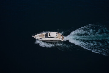 A large white yacht moves on blue water, side view, top view. White yacht moving on the water making a white trail looking like air.