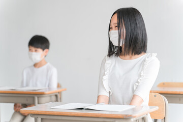 学校の教室でマスクをつけながら授業を受ける小学生
