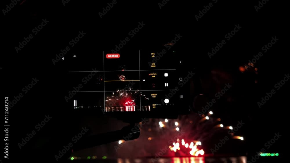 Poster cameras lined up in a row in front of a pyrotechnic display at a beachfront during a fireworks festi