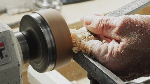 old man using a lathe and chisel to turn and cut a wooden disk