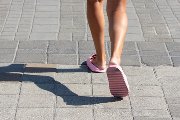 The legs of a girl in flip-flops walking on the paving slabs