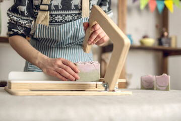 Women's hands cut homemade natural soap on a professional wood cutter. A means of eco-friendly hygiene
