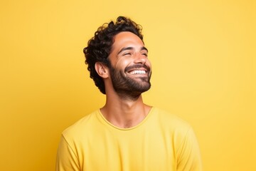 Portrait of a handsome young man laughing and looking up over yellow background