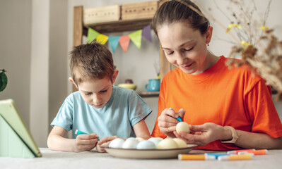 Fototapeta premium Happy Easter with your family. Mom and son are preparing for spring Easter by cheerfully coloring holiday eggs