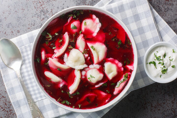 Old Polish beetroot borscht with traditional uszka dumplings stuffed with cabbage and mushrooms close-up in a bowl on the table. Horizontal top view from above