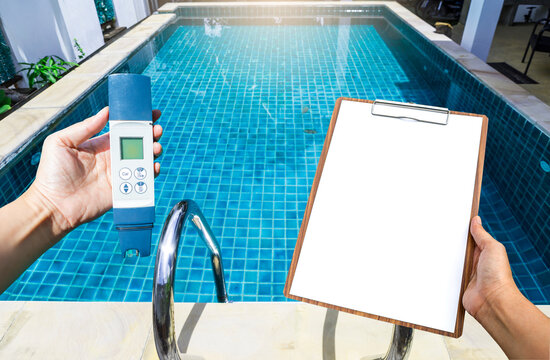 Digital water tester and blank white paper on wooden clipboard in girl hand over clear blue swimming pool water background, water quality check list, pool maintenance report, water analysis report