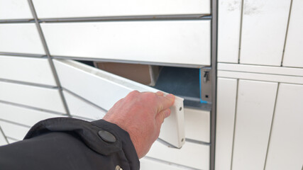 hand man with box open modern parcel locker with many postal boxes outdoors