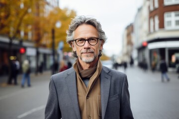 Portrait of a handsome senior man with grey hair wearing glasses and coat walking in the city.