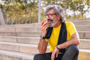 senior sports man rests eating an apple after a hard workout, concept of healthy and active...
