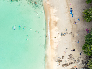 View from above, stunning aerial view of Banana beach, a beautiful white sand beach surrounded by palm trees and bathed by a turquoise water. Phuket, Thailand.