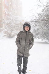 Fototapeta na wymiar A boy walks along a snowy street, it is snowing, blizzard and frost on a winter day