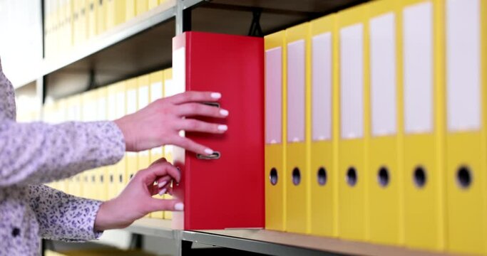 Female hand taking out red folder from shelf with yellow closeup 4k movie slow motion . Storage of important paper information concept